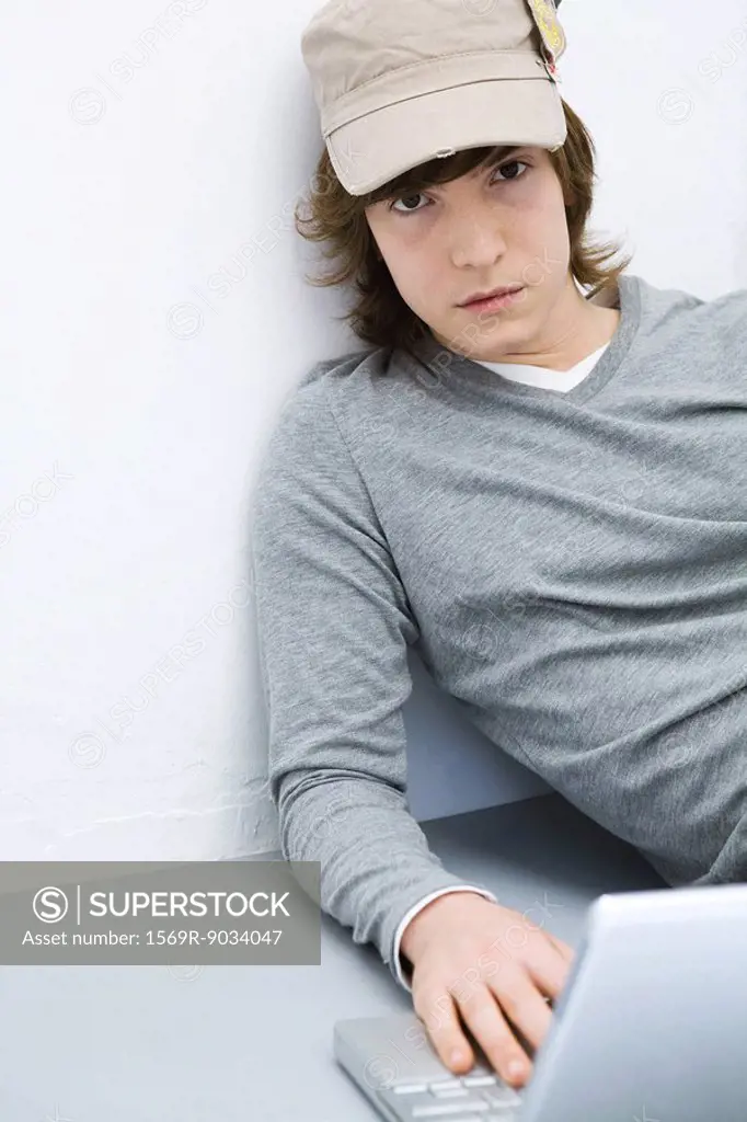 Young man sitting on the ground, using laptop computer, looking at camera