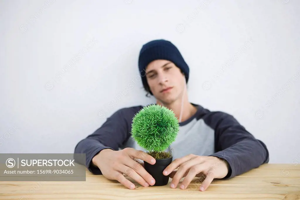 Young man sitting at table, holding bonsai, looking at camera