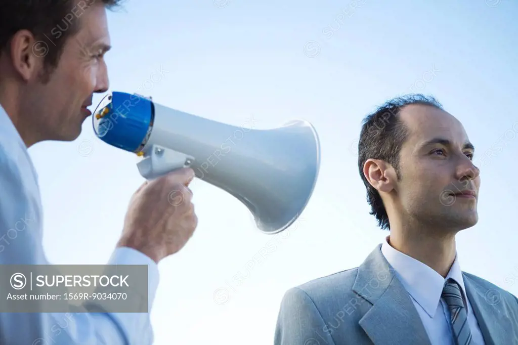 Businessman standing beside colleague, shouting into megaphone