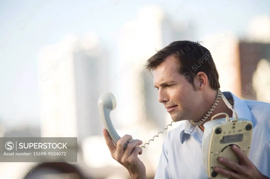 Man wrapping landline phone cord around neck, looking at receiver