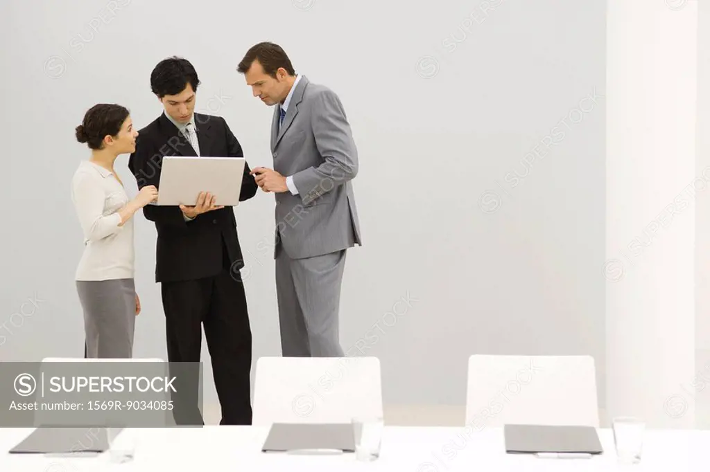 Business associates standing in conference room, looking at laptop computer together
