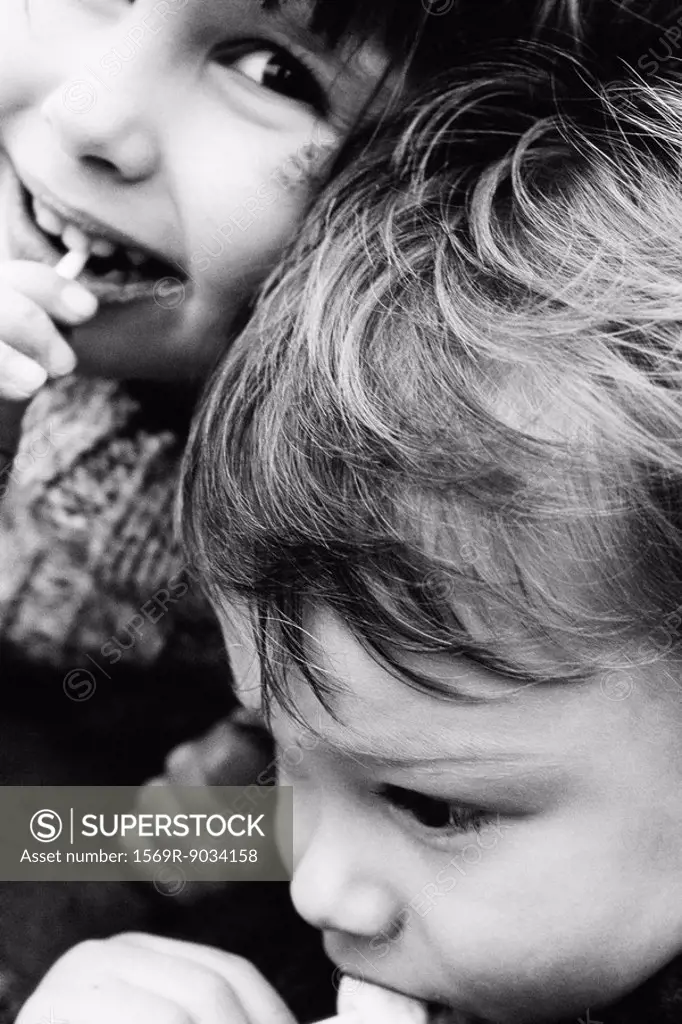 Two siblings eating lollipops, girl smiling at camera, close-up