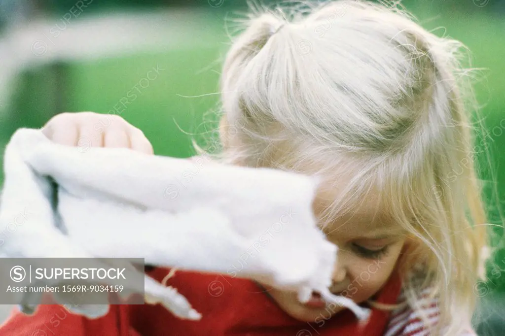 Little girl holding up kitchen towel, looking down, close-up