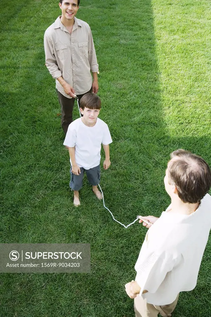 Boy playing jump rope with two men, smiling at camera
