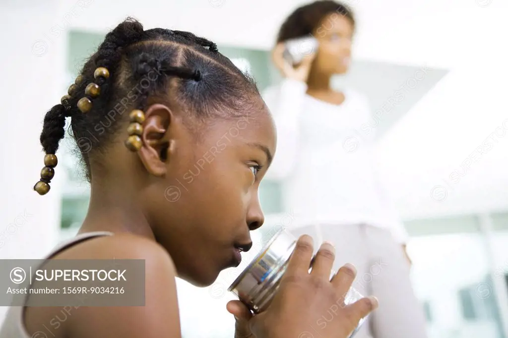 Little girl talking into tin can phone, mother listening in background, low angle view