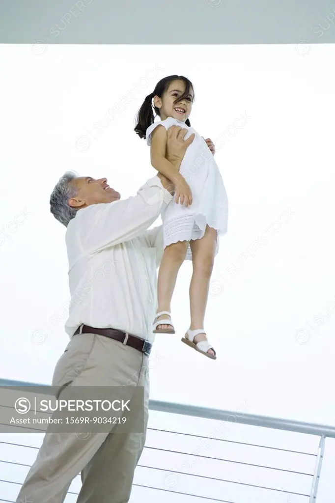 Grandfather holding granddaughter up in the air, both smiling, low angle view