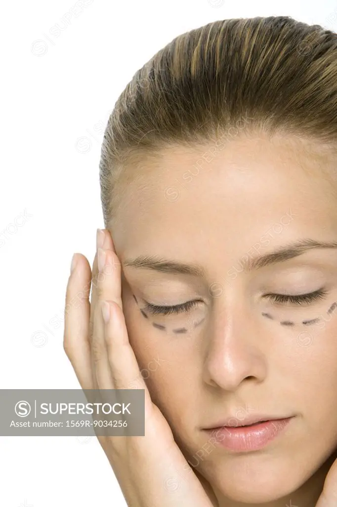 Woman with plastic surgery markings under eyes, holding face, eyes closed