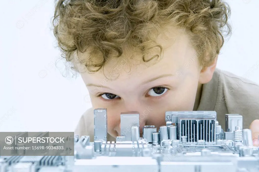 Little boy looking over circuit board at camera, close-up