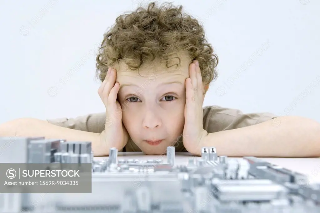 Little boy looking at circuit board, holding head, raising eyebrows