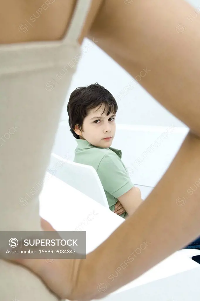 Boy sulking, looking over shoulder at mother in foreground with hand on hip