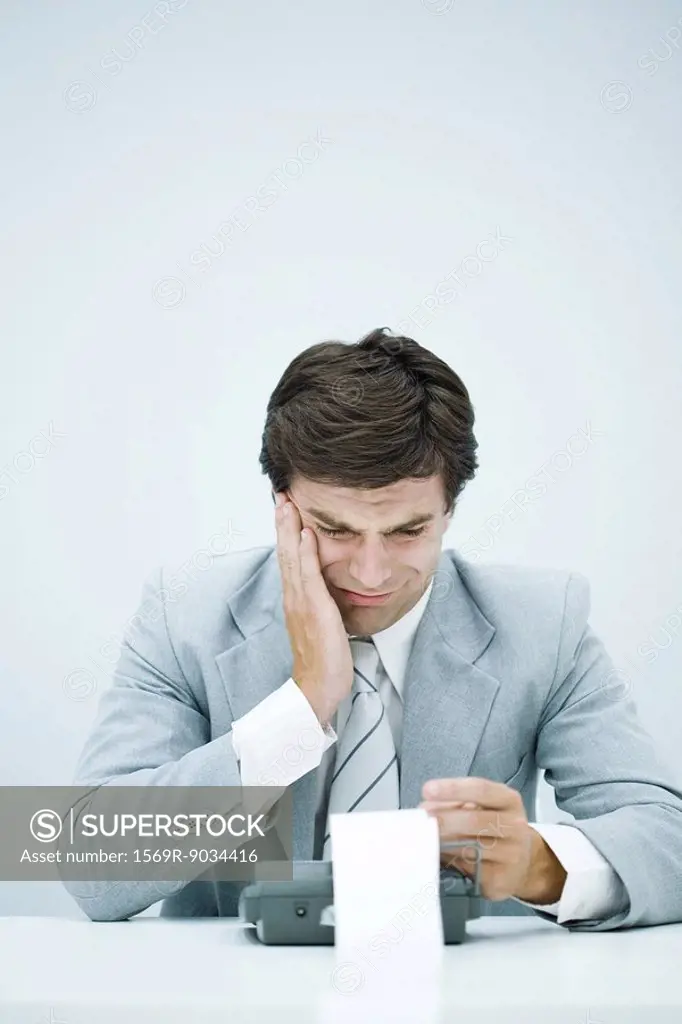 Man in suit looking at printout on calculator, holding head