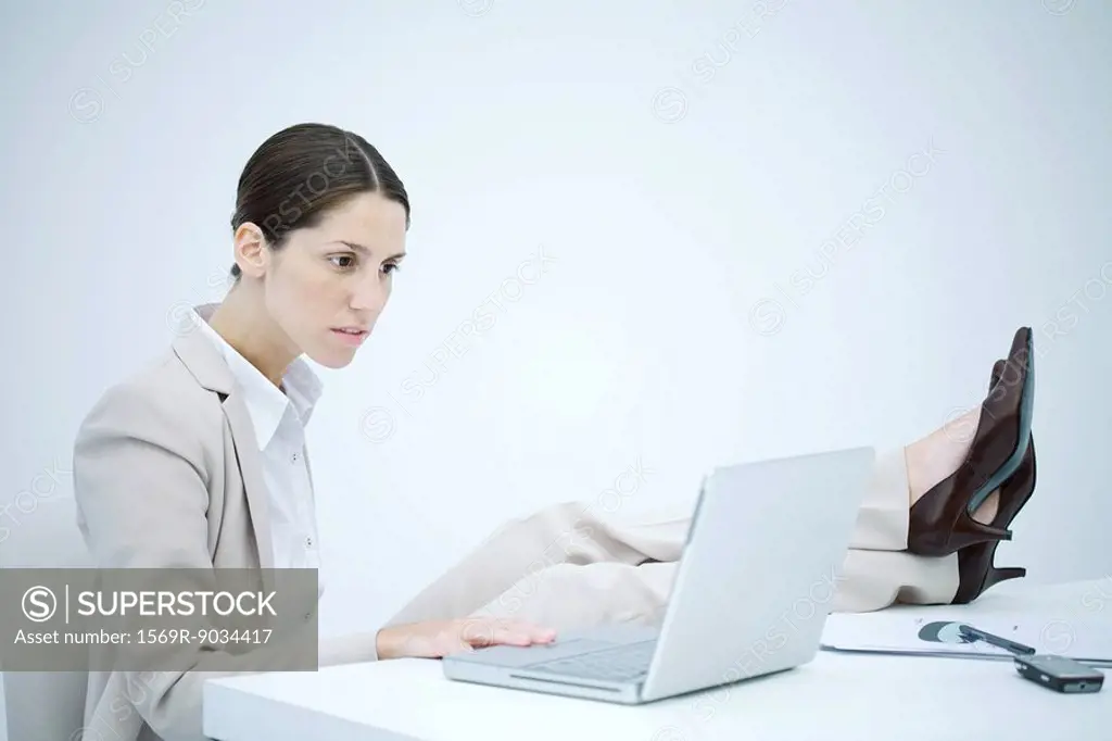 Businesswoman sitting at desk with legs up, using laptop