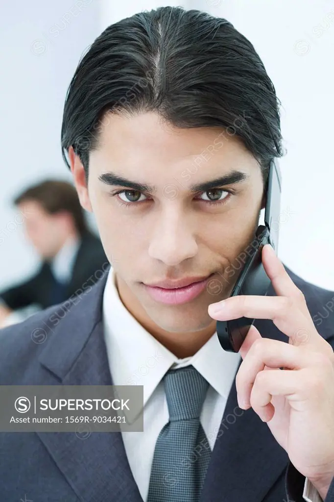 Young businessman using cell phone, smiling at camera, portrait