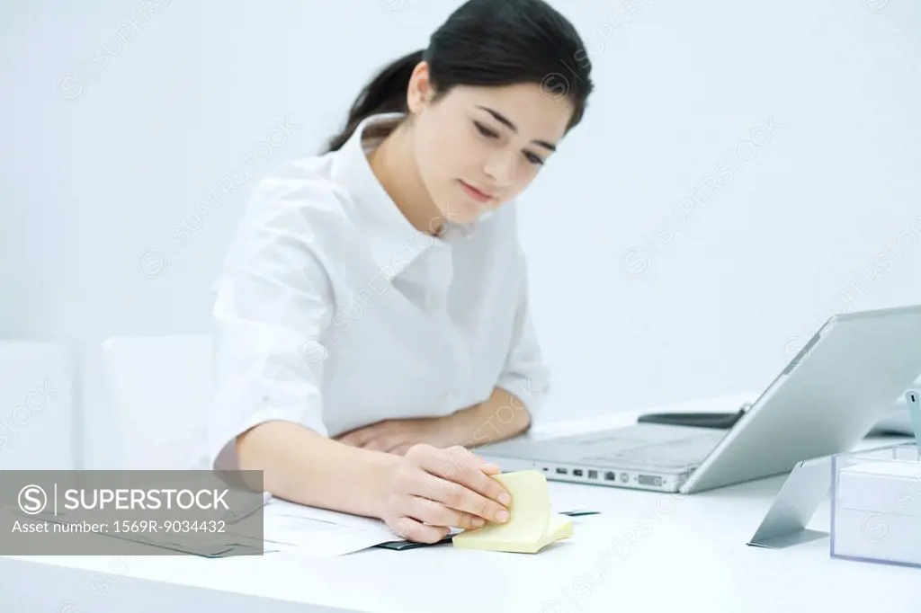 Young woman sitting at desk, flipping through adhesive note block