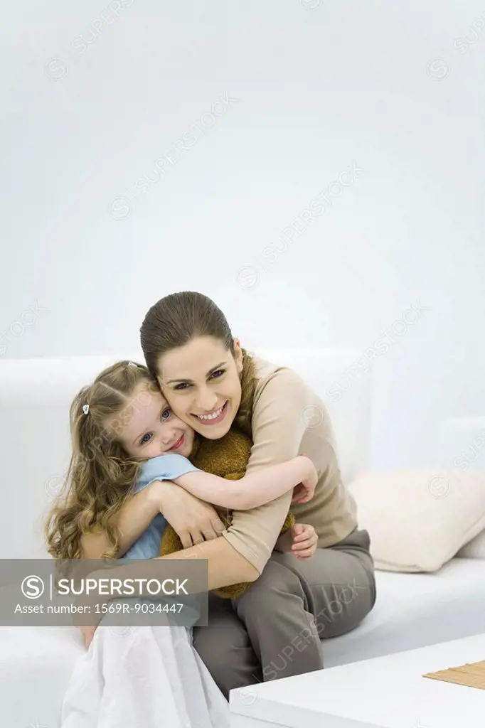 Young mother hugging little girl, smiling at camera