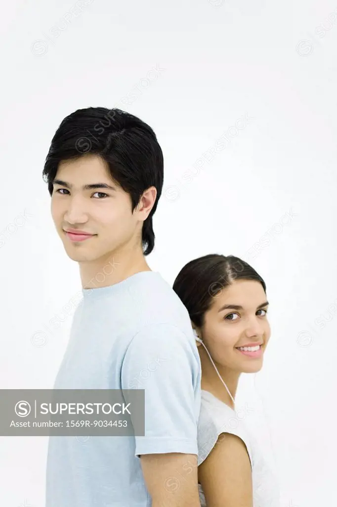 Young man and woman standing back to back, smiling at camera, portrait