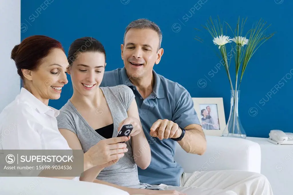 Mature parents and teen daughter looking at cell phone together, smiling