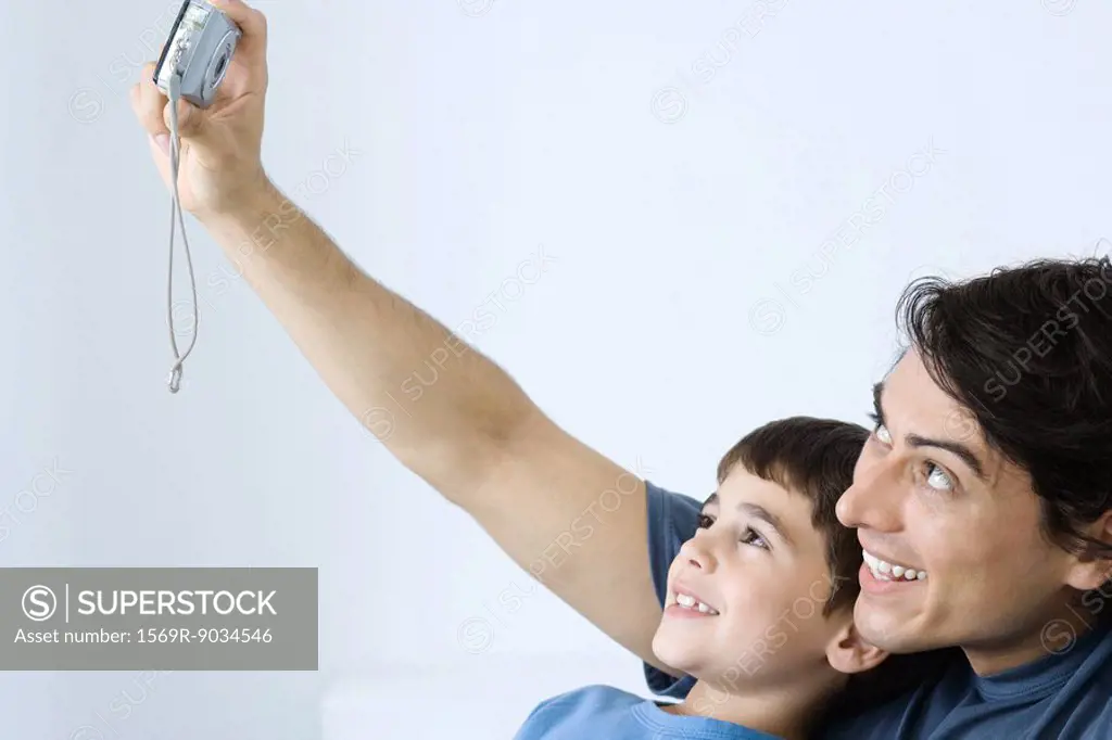 Man photographing self with young son, both smiling