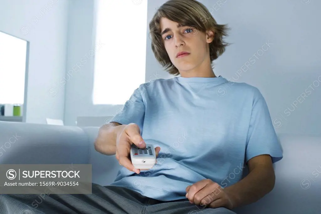Teenage boy sitting on couch, holding remote control, looking at camera