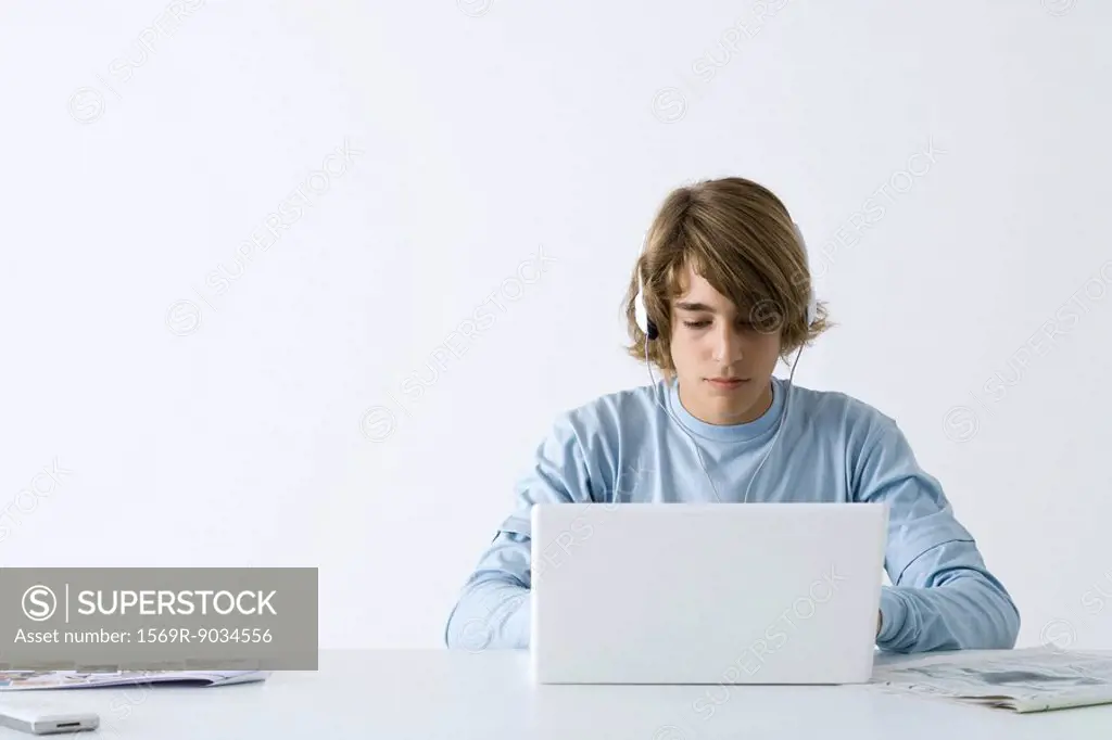 Teen boy using laptop computer, listening to headphones