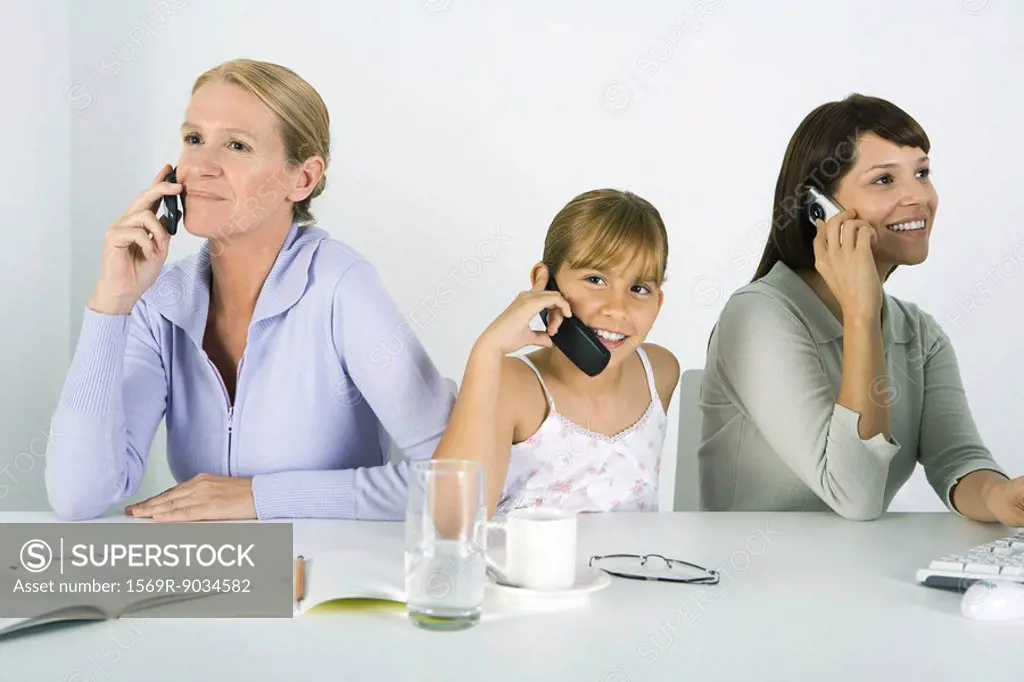 Mother and two daughters sitting at table, each using cell phone, smiling