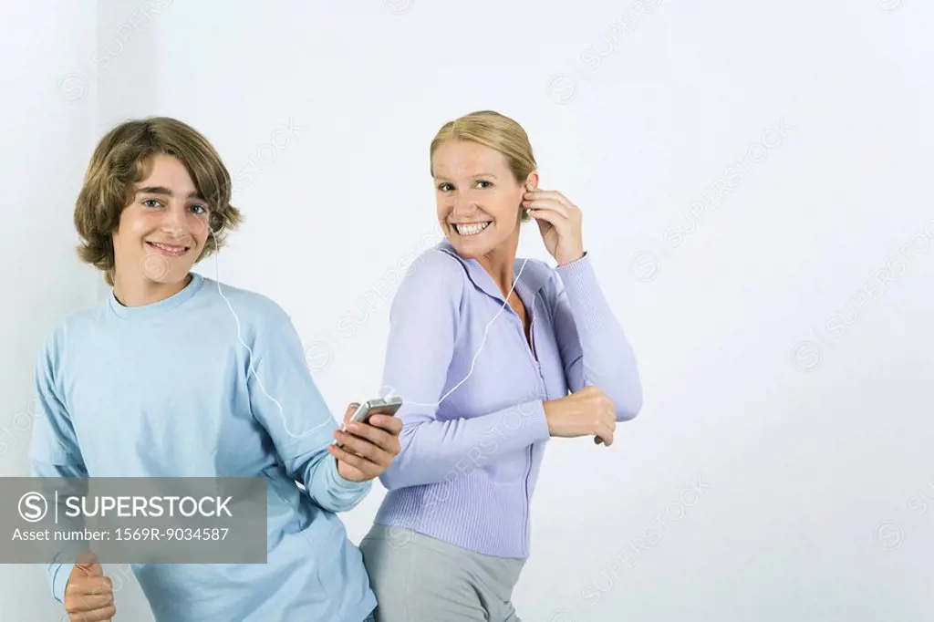 Mother and teen son listening to MP3 player together, dancing, smiling at camera