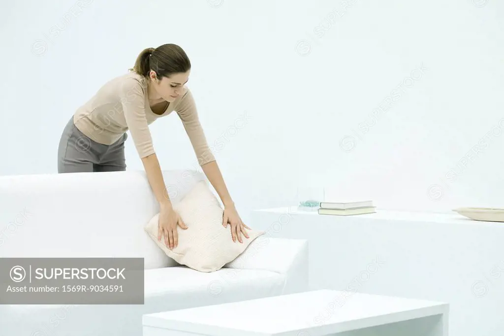 Woman leaning over couch, arranging pillow