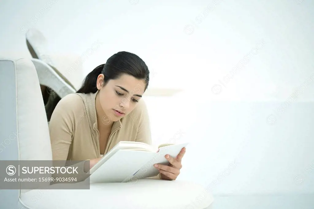 Young woman lying on couch, reading book