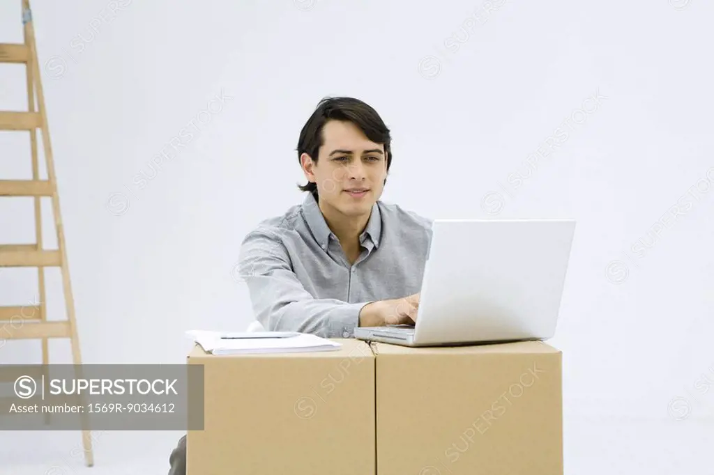 Man working on laptop computer, using cardboard boxes as makeshift desk