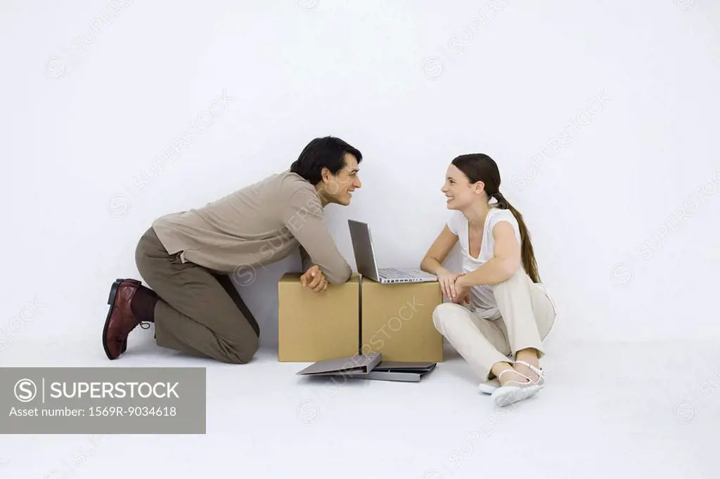 Couple sitting at makeshift desk with laptop computer between them, smiling at each other