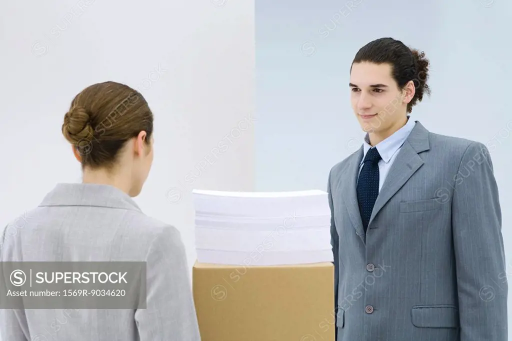 Young professionals standing face to face, documents stacked on cardboard box between them