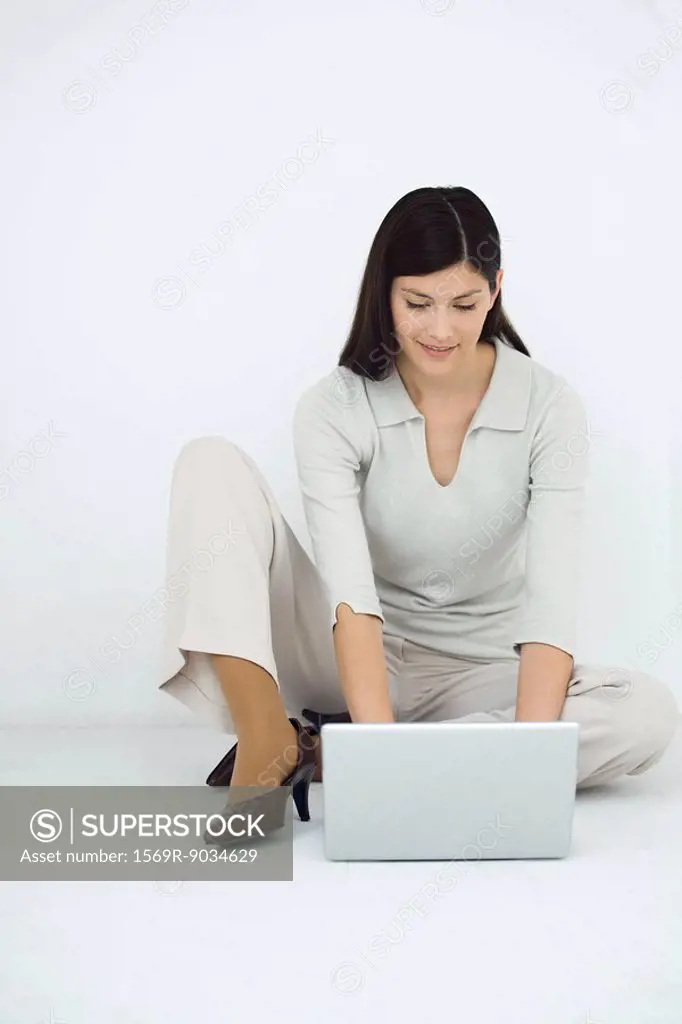 Woman sitting on the ground, using laptop computer, smiling