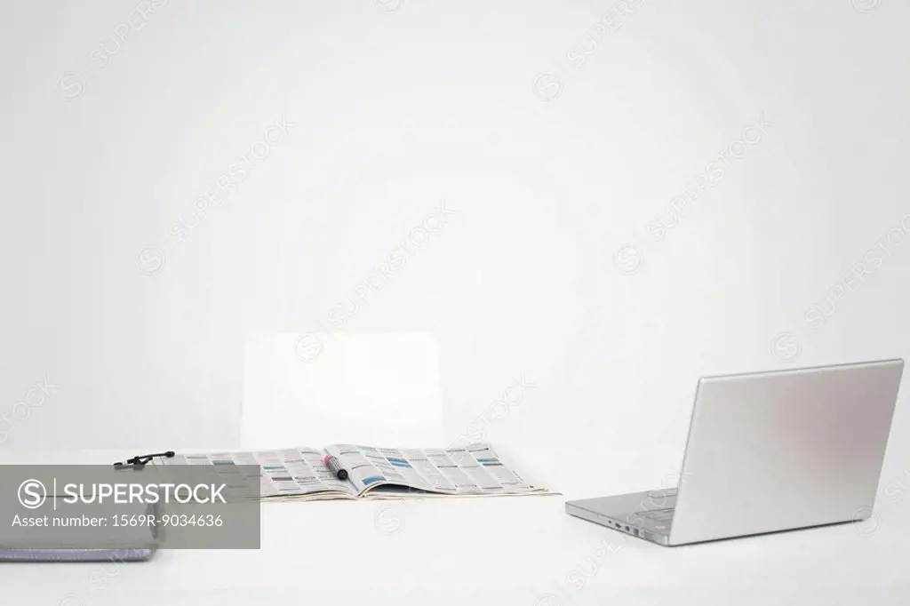Desk with laptop computer and open newspaper with circled listings