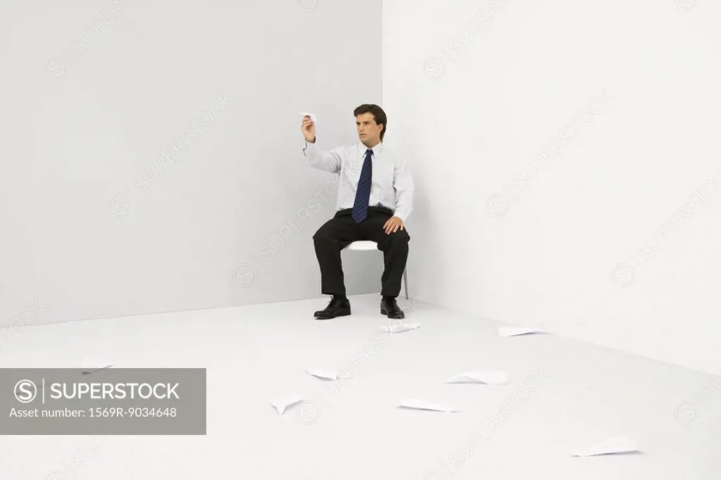 Male professional sitting in corner, throwing paper airplanes
