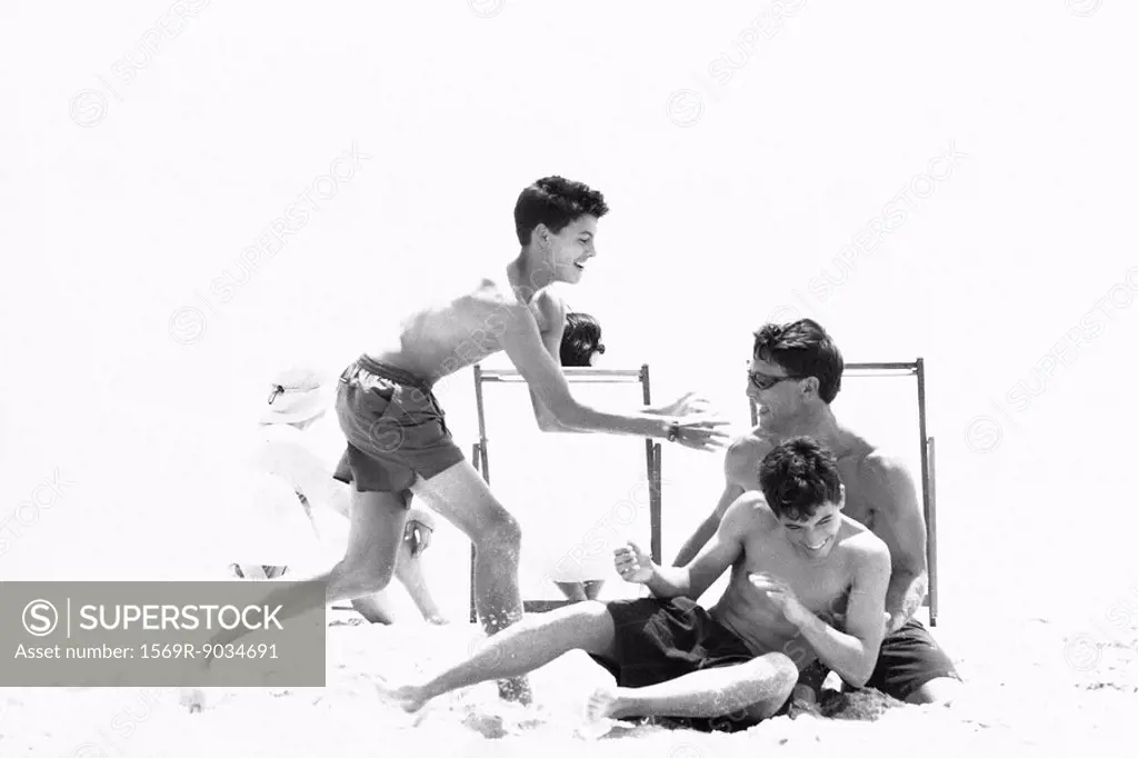 Man roughhousing on beach with teenage sons, black and white