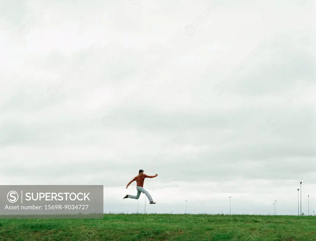 Man jumping on grassy field, in the distance