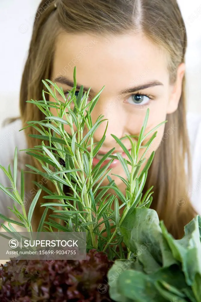 Young woman with veggies and herbs, looking at camera