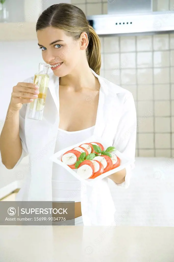 Young woman holding tomato and mozzarella salad, smelling salad dressing