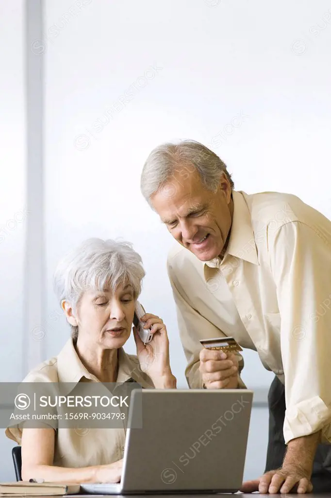 Mature couple making credit card purchase, using laptop and cell phone