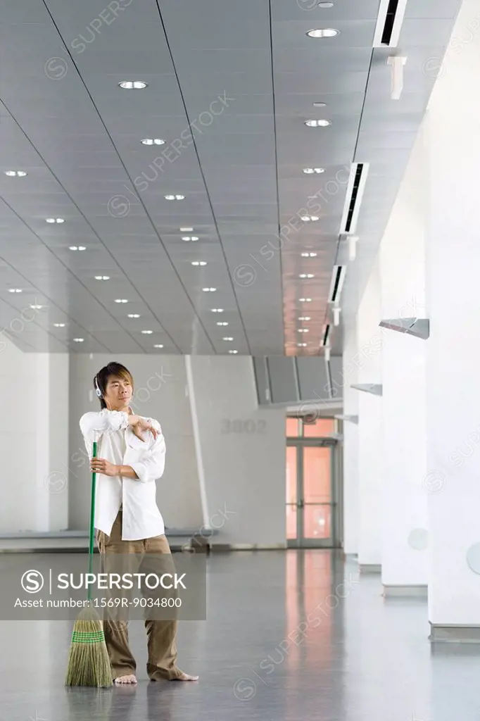 Man standing in lobby with broom, listening to headphones