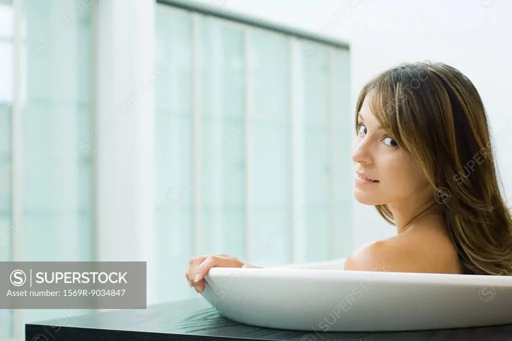 Woman taking bath, looking over shoulder at camera