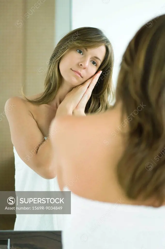 Woman standing in bath towel, looking at self in mirror