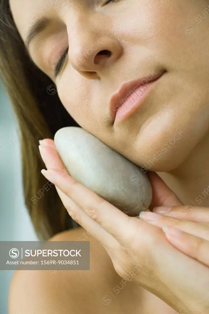 Woman holding smooth stone against face, cropped