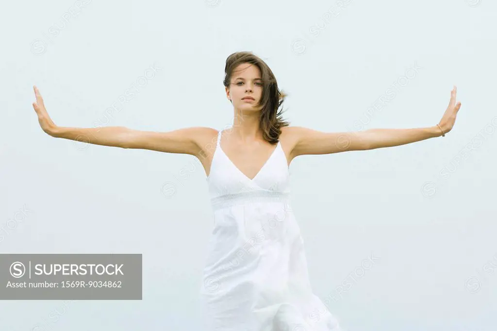 Young female standing in dress, holding arms out to sides while wind blows