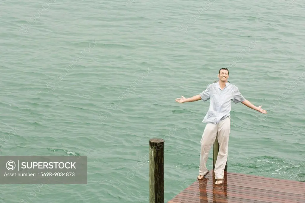 Man leaning against dock post, getting wet, arms out, smiling at camera