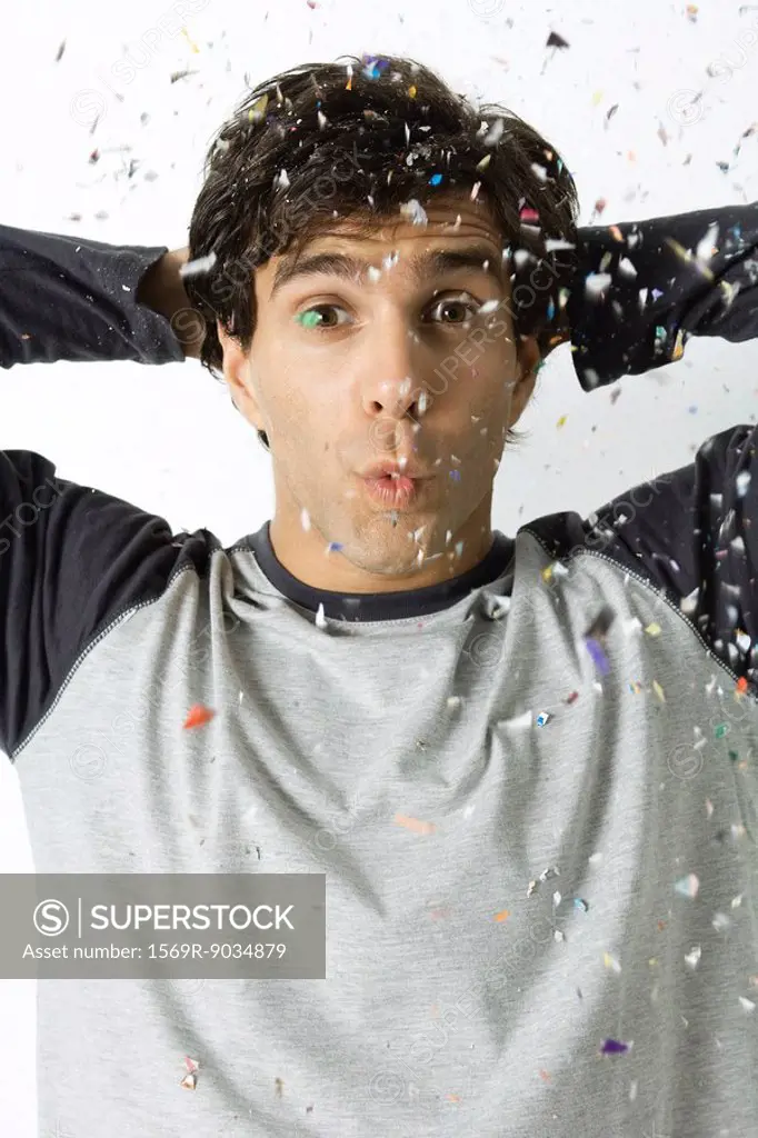 Man among falling confetti, puckering lips, looking at camera