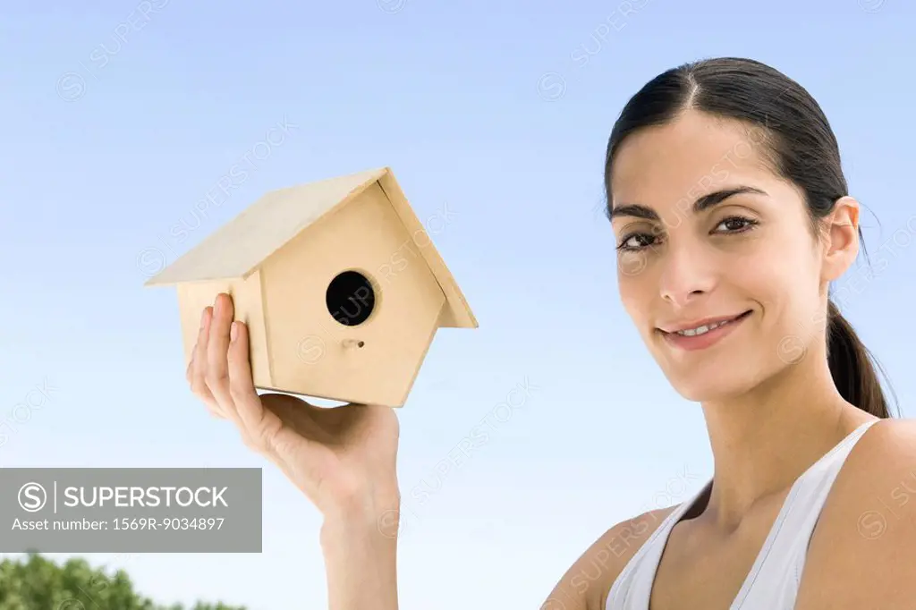 Woman holding up birdhouse, smiling at camera