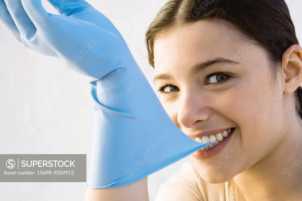 Woman pulling off rubber glove with teeth, smiling at camera