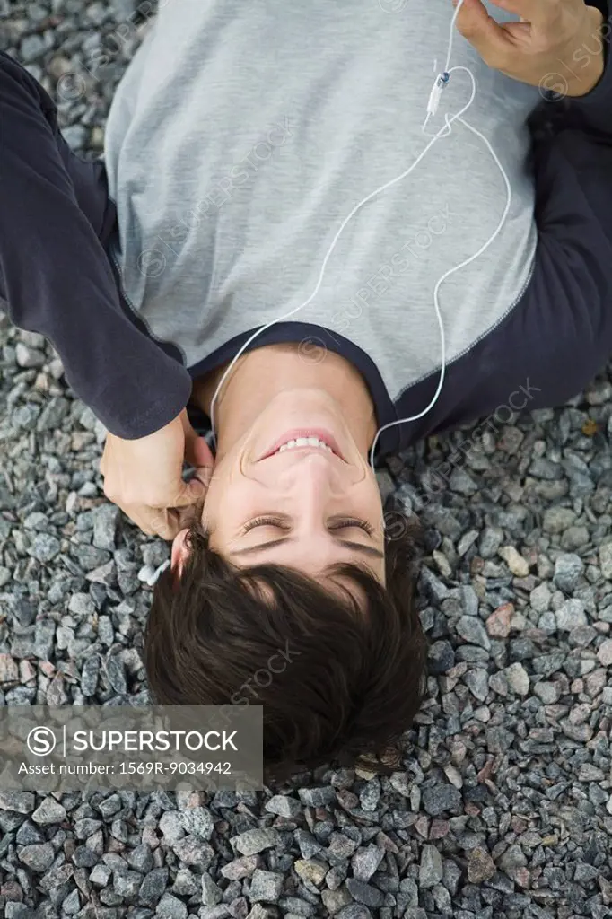 Young man lying on gravel, listening to earphones