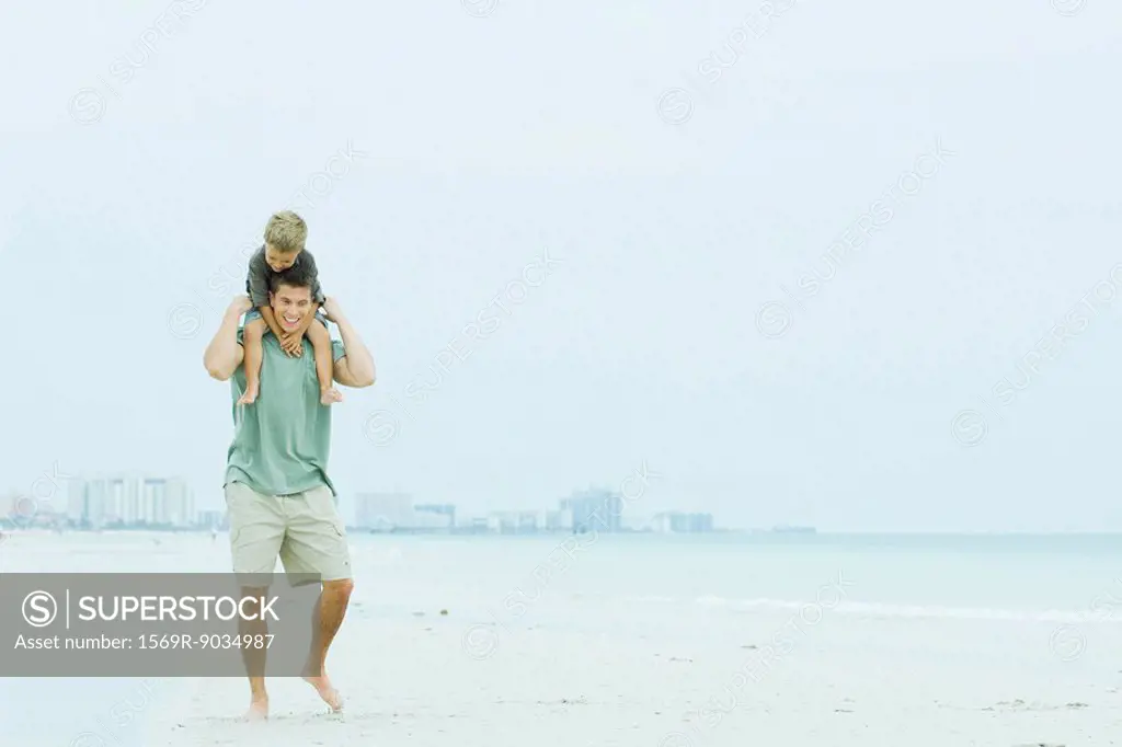Father and son walking at the beach, man carrying boy on his shoulders